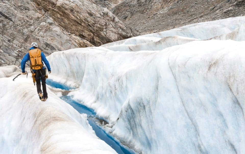 Un professionnel équipé avance avec prudence le long d’une crevasse, symbole des risques aérauliques à contenir et de la conformité qu'il doit garantir